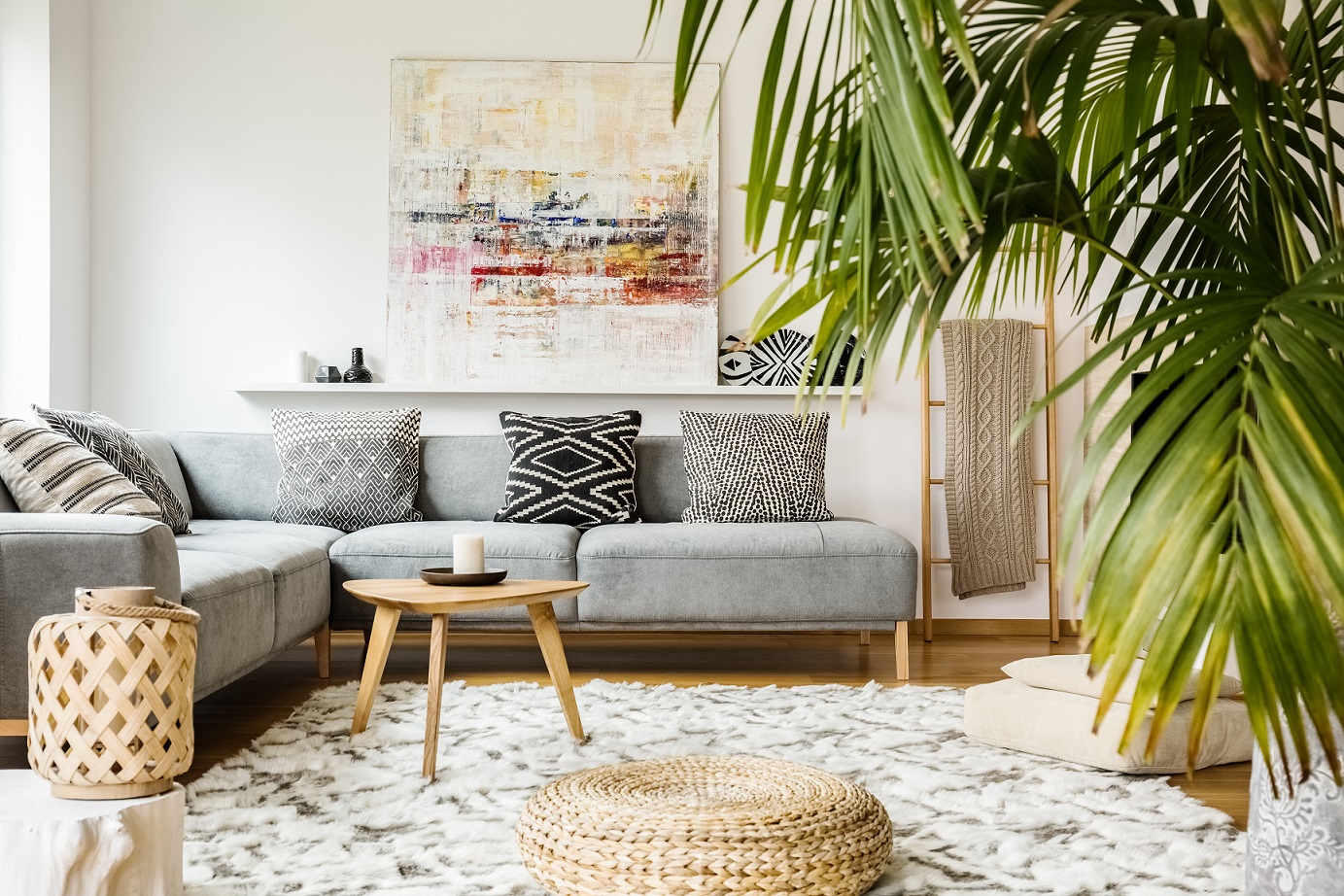 Pouf and wooden table in modern living room with painting above grey corner couch. Real photo