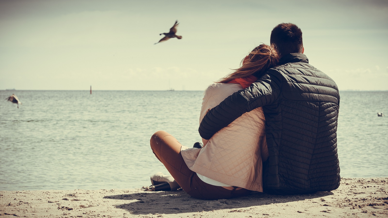 loving couple spending leisure time together at beach hugging rear view