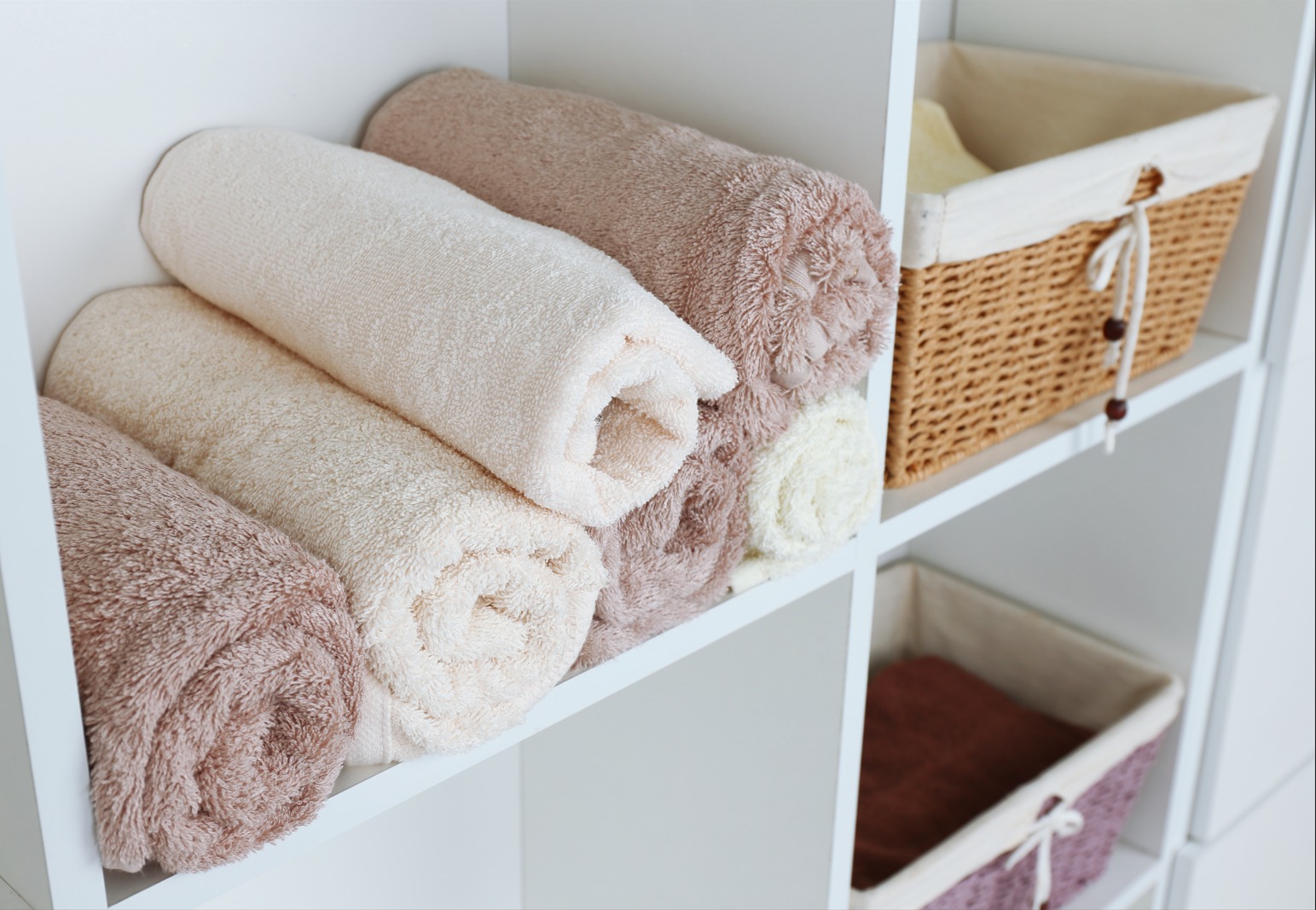 towels neatly rolled into a closet with woven baskets next to them